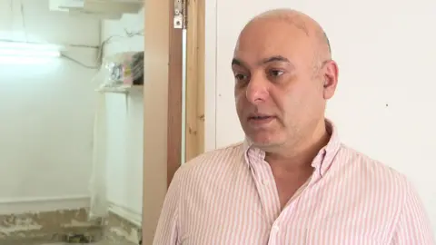 Mohamad Zakaria, a middle-aged bald man, in a striped shirt in a flood-damaged shop.