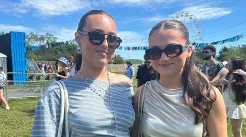 Two young women successful sunglasses grin astatine the camera connected a euphony festival site.
