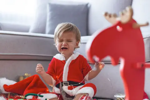 Getty Images Upset child in santa outfit with rocking horse crying