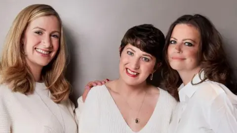 Three woman pictured in a line wearing white jumpers, Dame Deborah a white shirt. Bland has shoulder length blonde hair, Mahon short brown hair and Dame Deborah has long brown hair