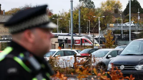 রয়টার্স একজন ইউনিফর্মধারী পুলিশ অফিসার হান্টিংডন স্টেশনের কাছে দাঁড়িয়ে আছে, যেখানে মধ্য দূরত্বে একটি LNER ট্রেন দেখা যায়।