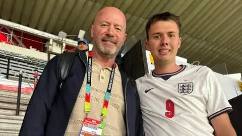 Owen Roberts Alan Shearer is wearing a dark jacket, light jumper and jeans. He is standing next to Owen Roberts who is wearing a white England top with a red number nine on it. 