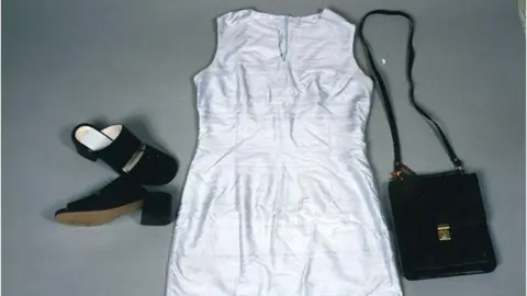Avon and Somerset Police An example of the clothing Melanie was wearing that night, laid out on a grey table. There are black suede shoes with a small chunky heel, a white dress and a black handbag with a skinny strap and a gold clasp. 