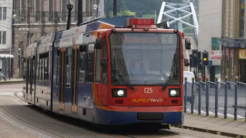 A red and blue tram travels towards the camera through the centre of Sheffield.