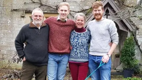 Debs Goodenough The couple are pictured arm in arm with their two grown up sons. It looks like they are outside a church building. A dog is on a lead but out of shot.
