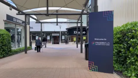 Amber Ward / BBC A shopping centre is lined by hedges and billboards.