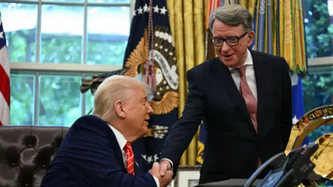 AFP via Getty Images Mandelson and Trump. both suited, shake hands and smile at each other in the Oval Office, which has gold curtains. 