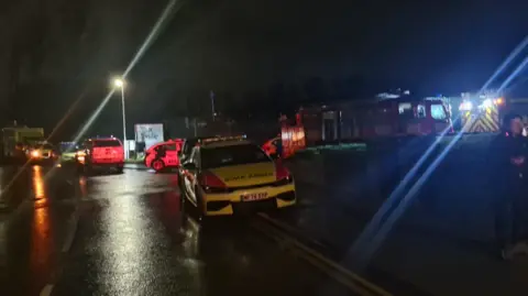 Lancashire Police A fire engine lights up a dark street with its lights with a police car in the foreground