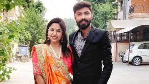 Nirav Patel A picture of Vaibhav Patel and Jinal Goswami. Jinal is wearing a traditional dress and Vaibhav a black suit jacket with a grey open neck shirt.
