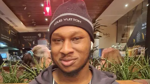 Leicestershire Police Khaleed Oladipo wearing a black hat and zip-up jacket, smiling.
