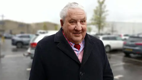 A white haired man in a black overcoat 