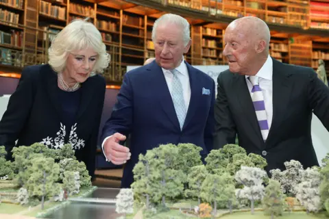 REUTERS/Toby Melville/Pool Queen Camilla, King Charles and Norman Foster look at a to-scale model of St James's Park and the design planned for the memorial. They are in the British Museum's library room, so there is a towering wall of books behind them.