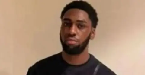 Met Police Jordan Kukabu, pictured in front of a plain wall and wearing a black top