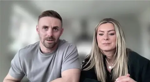 A screenshot of Adam and Tayah Aveling, he has short brown hair and short beard. She has long blonde hair.