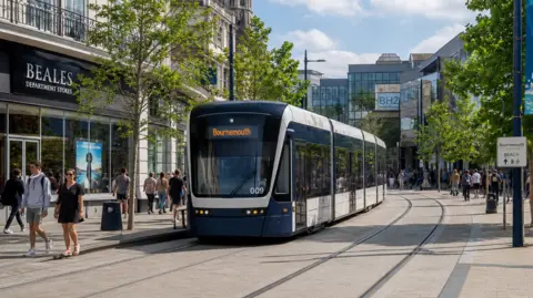 A computer-generated image of a tram making its way through a town centre. The tram has an electronic sign reading "Bournemouth" on the front and is travelling along a track that curves past the view of the camera. People can be seen walking around in the area surrounding the tram.