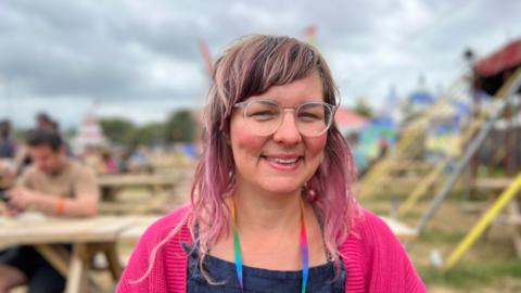 Women with pink cardigan smiling, with tables and tent behind her.