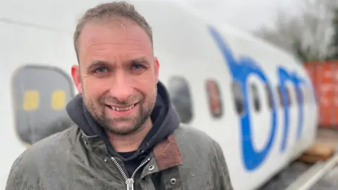 Man in a waterproof jacket in front of a white plane fuselage