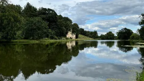 Surrey Ambler/BBC A river reflecting trees and a house, all under a blue sky