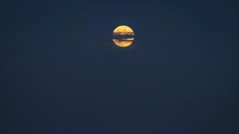 Hang Ross An orange moon in the distance behind a thin line of dark cloud across its centre