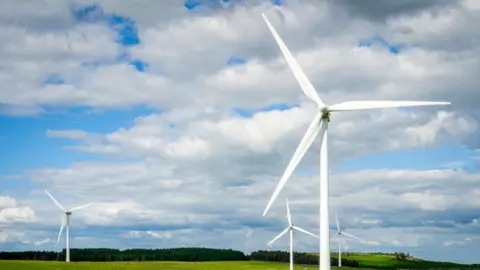 Getty Images A stock image of four large wind turbines in a field. There is a blue sky which is covered by some clouds.