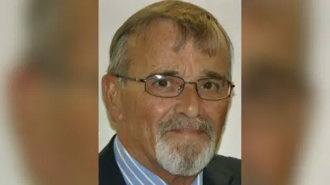 Family photo A man with a grey goatee beard, thin glasses and short grey hair 