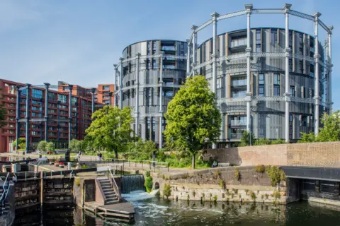 Getty Images Two skeleton structures of gas holders with new housing built inside, beside more traditional housing sited beside a canal lock in London.