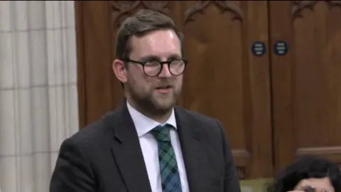 Parliamentlive.tv Henley MP Freddie van Mierlo speaking at a Westminster Hall debate - he is wearing a dark grey suit and checked green and blue tie. 