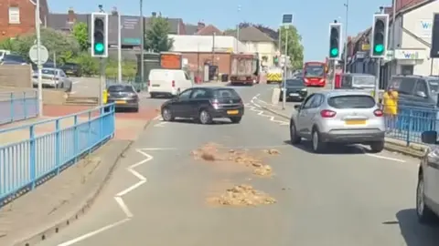 Staffordshire Events Two piles of brown-coloured offal on a main road, just before a traffic-light controlled pedestrian crossing. Cars can be seen manoeuvring 