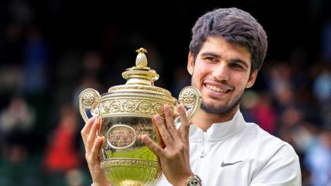 Carlos Alcaraz smiles as he lifts the Wimbledon trophy