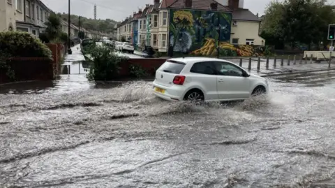 A white car driving through flooding on a residential street