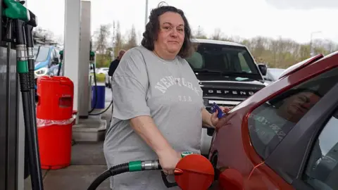A woman looks at the camera as she fills herred  car at a petrol station in Derby