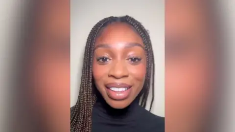 A woman with braids and a black turtle neck top smiles