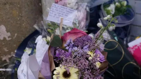 Purple, yellow and red flowers at the crime scene with a note with voice speech "Quiet in paradise Layton". 