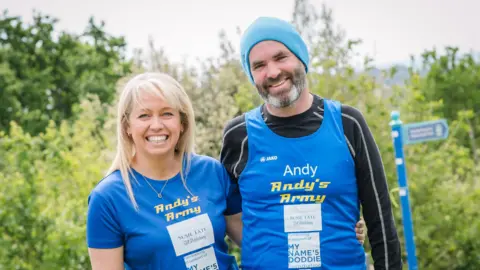 My Name’5 Doddie Foundation Mr and Mrs Vaughton wearing bright blue running tops and are standing outside.