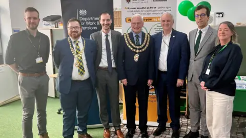 Six men and a woman stand in a semi circle smiling at the camera
