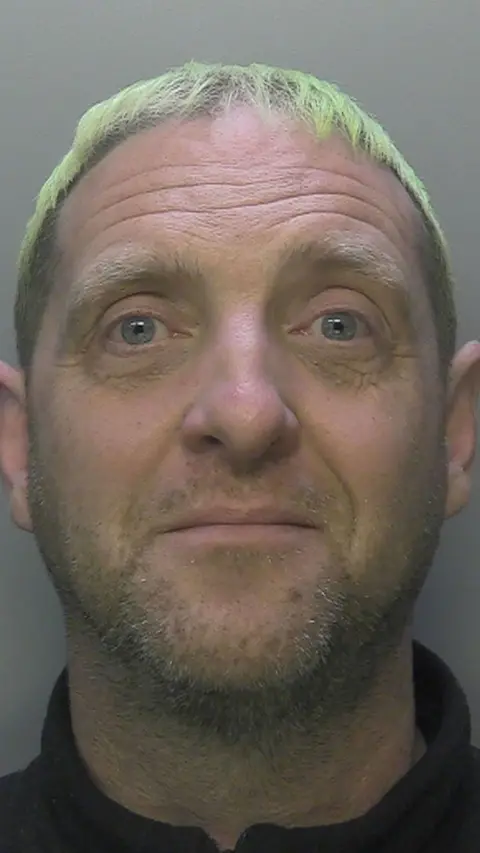 A police mugshot of a man with green hair.