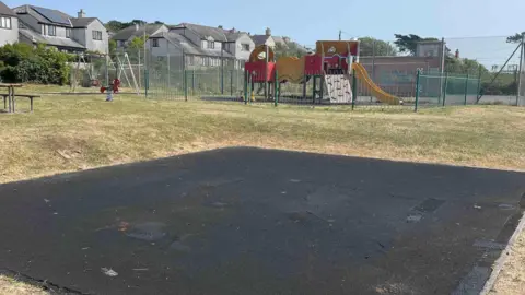 An empty patch of ground in the middle of a play area where swings and a roundabout once stood.