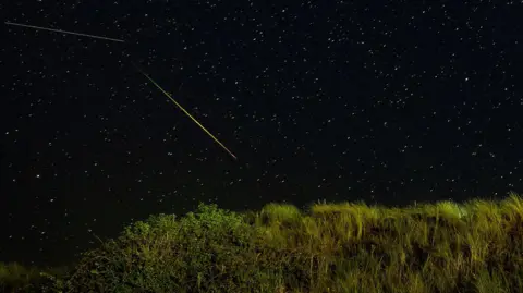 PA Media The Perseid meteor shower reveals dots (stars) in the sky and two long lines of light or shooting stars. 