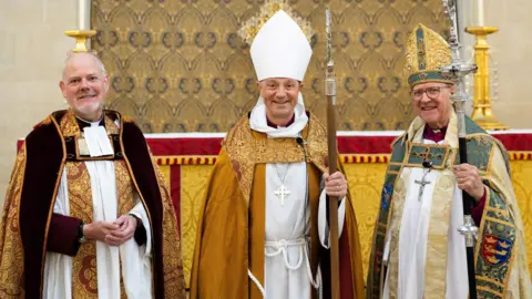 Keith Mindham Joe Hawes, Mike Harrison and Martin Seeley stand in a row wearing their Anglican Pontifical vestments. They are all smiling at the camera and standing in front of an altar. 