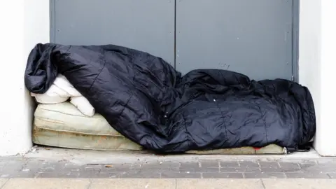 Getty Images Stark image of a black sleeping wag on top of a dirty mattress, in a doorway, against a grey wall