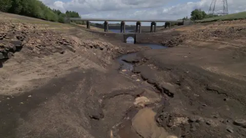 A bare reservoir bed with a bridge in the background