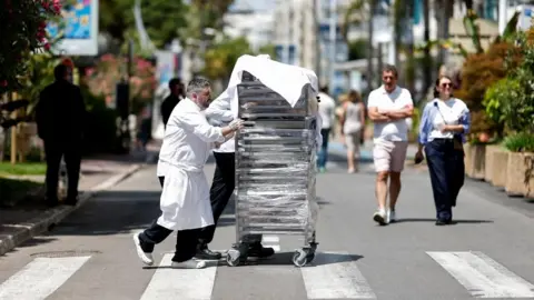 Reuters A man pushes a trolley carrying food from a hotel on a road as passers-by look on, following a power outage in Cannes.