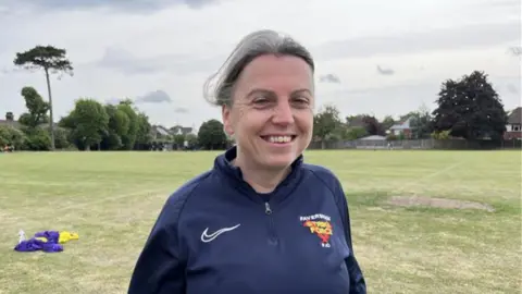 A woman wearing a navy blue coat smiling at the camera while stood in a field