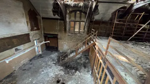 Dilapidated inside of an old building with wooden stairs and rubble on the ground