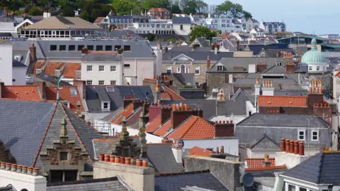 A skyline in Guernsey with a range of different homes and rooftops, some with grey slate tiles and others with red roofing tiles.