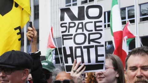 Getty Images Anti-racism protestors. One is holding a sign saying "no space for hate"