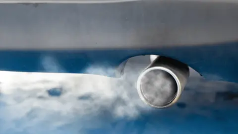 Reading Borough Council Stock image of a car exhaust. It is silver, at the back of a car and there is white smoke around the vehicle and a blue tint to the image.