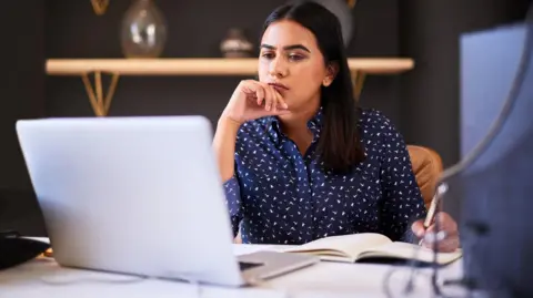 Focused businesswoman writing in a notebook while working alone on a laptop in an office. One female only thinking before making notes in her diary and planning online while working at her desk - stock photo