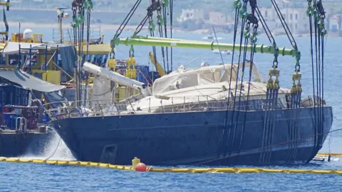 Peter Byrne/PA Wire A ship being held on its side by a crane with water being pumped out of it
