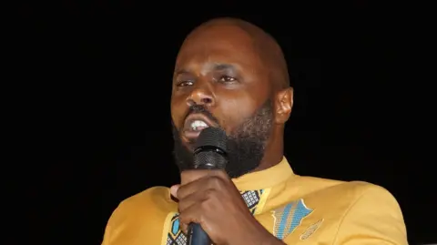 Pan-African Emergency movement leader and anti-colonialist Beninese activist Kemi Seba in yellow jacket, holding a microphone